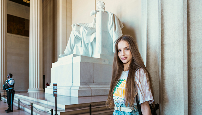 A young woman in a Mason tee shirt sits in front of the statute of Abraham Lincoln at the Lincoln Memorial.