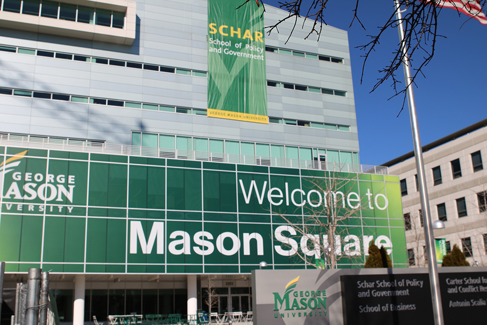 A silver building with green George Mason University signs is seen in streetscape.