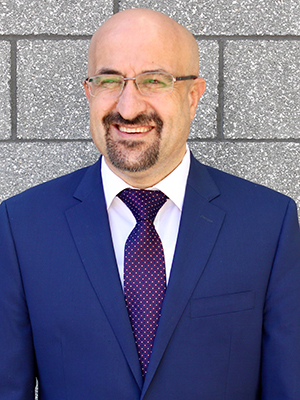  A bald man with a short beard in a blue jacket and purple tie smiles.