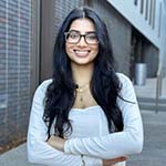 A woman in a white shirt stands outside while smiling