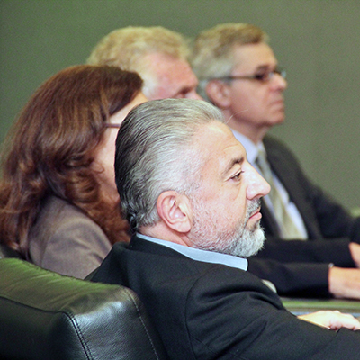 A man with silver hair in a dark jacket sits next to three others who look to their right.