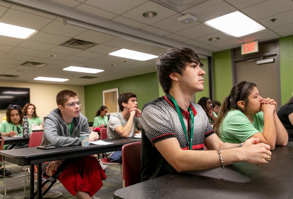 Undergraduate students listen sit at desks in a classroom.