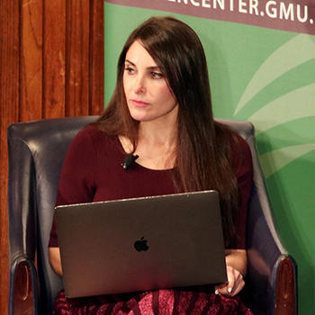 A woman in a maroon outfit sits in a black chair with an open laptop on her lap.